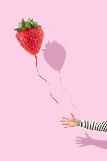 一只手在亮粉色背景上抓着一个红色草莓气球的垂直镜头图片下载