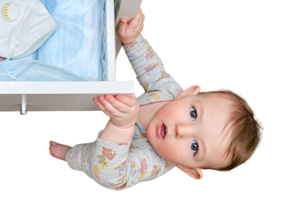 一个蹒跚学步的男婴撕开了一个装满医用口罩的衣柜抽屉，这些口罩孤立地放在白色背景上。孩子拿着柜子的门把手，一个小孩子图片下载