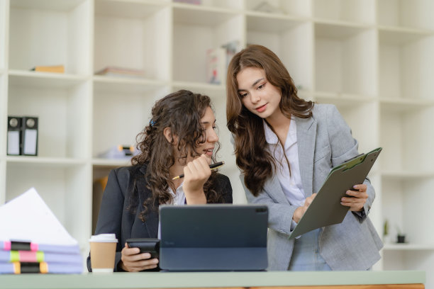 年轻有魅力的白人老板兼助理，在办公室的桌子上放着图纸和平板电脑，听着金融业务咨询图片下载