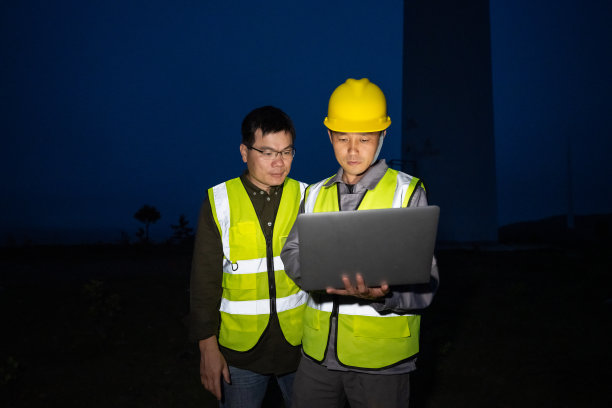 晚上，两名男性工程师用笔记本电脑在风力发电场工作图片下载