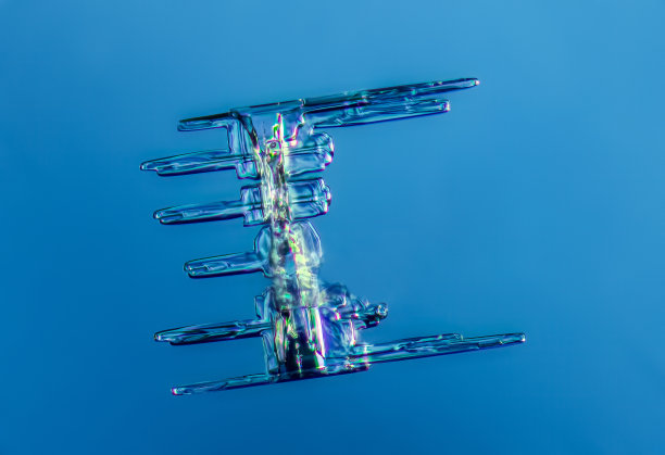 真实柱状雪花在高倍放大。微距照片的小边雪水晶，雪花发光在深蓝色背景图片下载