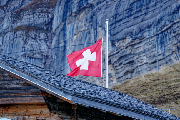 在伯尔尼州阿克塞尔普的缆车山站挥舞瑞士国旗，这是一个蓝色多云的秋日。图片下载