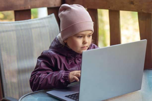 一个可爱的小女孩坐在乡间别墅的露台上，用笔记本电脑进行在线学习或交流图片下载