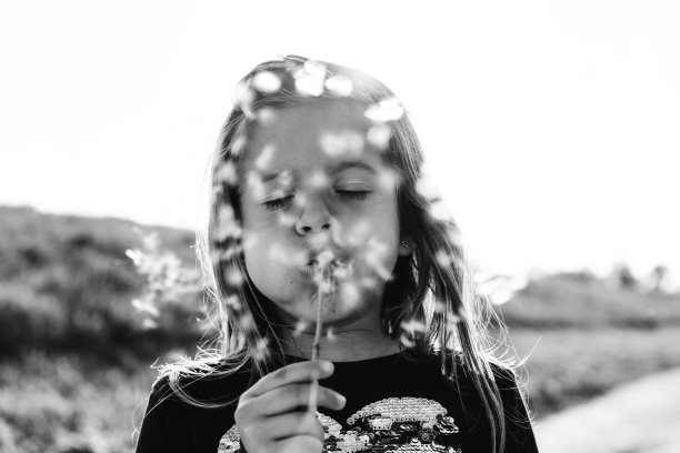 可爱的小女孩蒲公英花在农村在一个春天阳光明媚的日子-女性孩子有乐趣和吹蒲公英的种子户外-童年的概念-黑白编辑图片下载