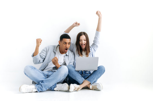 快乐兴奋的多种族男女，惊讶地看着笔记本电脑的屏幕，为好消息而高兴，胜利，成功，开心地微笑，手势，同时坐在地板上白色孤立的背景图片下载