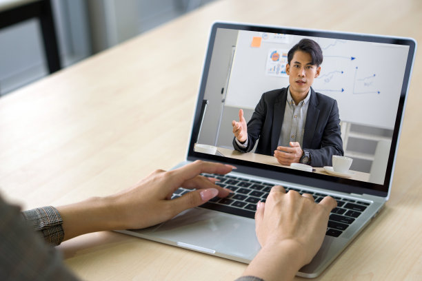 一个穿着格纹西装的女商人坐在办公室的桌子前，用笔记本电脑键盘打字，与投资顾问进行网络摄像头会议。图片下载