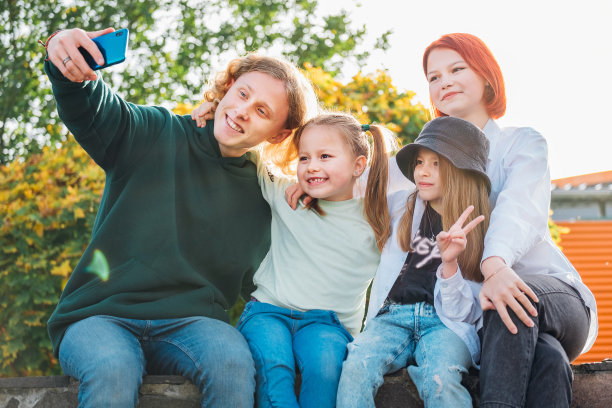 这是三姐妹和弟弟用现代智能手机相机自拍的照片。无忧无虑的少年快乐，童年时光和现代科技的概念形象。图片下载