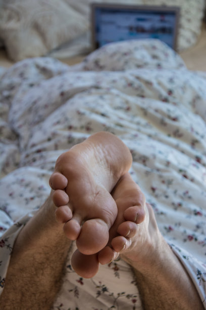 带着笔记本电脑躺在床上的男人专注于脚图片下载