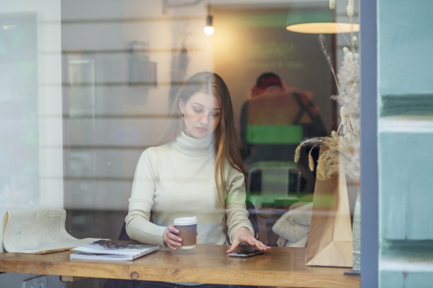 年轻的成年女子正在咖啡馆里看杂志，喝着热饮。图片下载