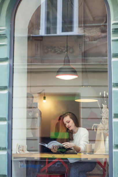 白天，女人坐在现代咖啡馆的窗边。女孩正在看一本有趣的书。图片下载