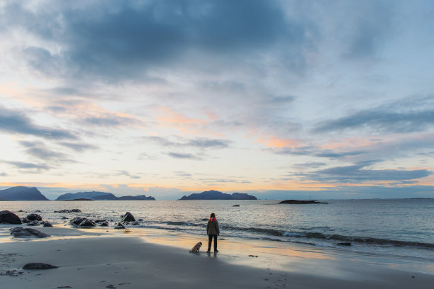 在挪威的海边，一位女士带着一只狗凝视着美丽的日落图片下载