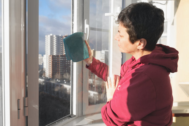 戴着橡胶手套的中年黑发女子在她公寓的阳台上用抹布擦窗户。图片下载
