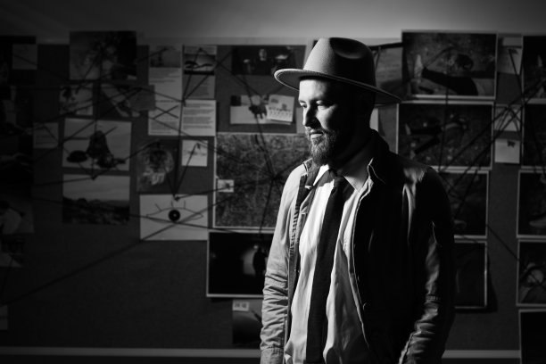 戴着帽子、穿风衣打领带的年轻特工，深夜在办公室工作的侦探，证物板背景，黑白照片图片下载