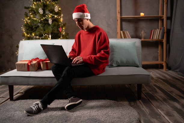 快乐的男顾客，购物者庆祝圣诞节。阿拉伯人在圣诞老人帽子使用笔记本电脑在冬季12月销售网上购物，自由职业者在家里工作图片下载