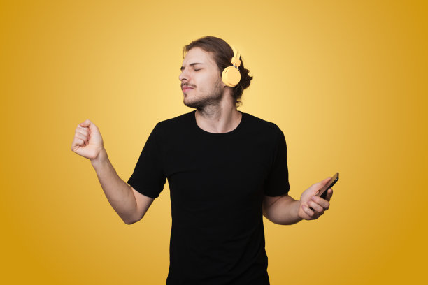 年轻人戴着耳机，听着最喜欢的音乐，闭着眼睛，与黄色背景隔离。快乐的生活方式图片下载