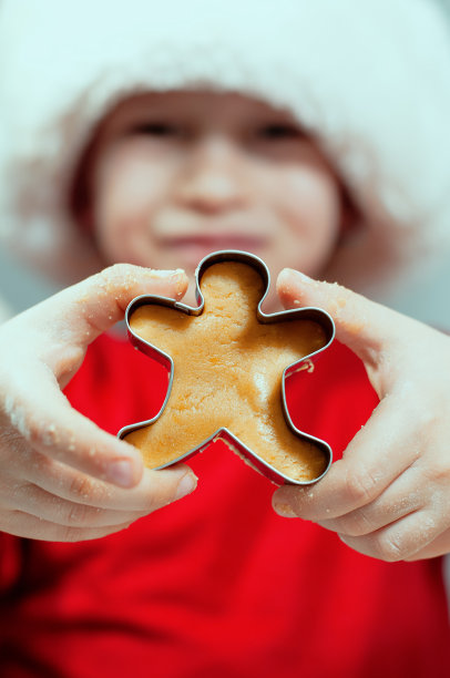 一个穿着红色毛衣、头戴新年帽的孩子拿着一个前景是姜饼人的模具。高质量照片图片下载