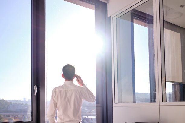 商务环境——商务人士站在办公室靠窗用手机打电话图片下载