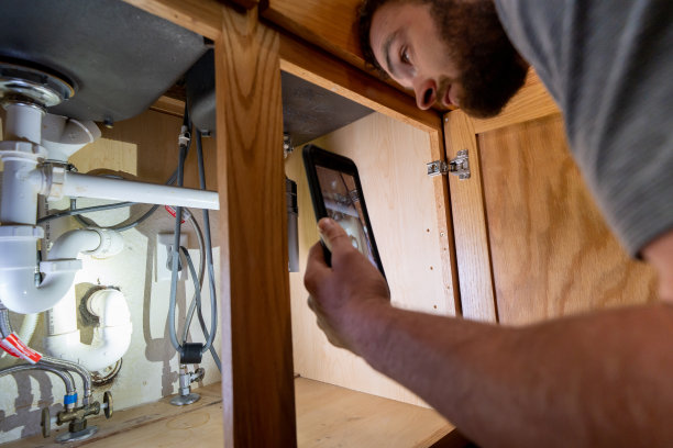 年轻的大胡子财产检查员在现代家庭住宅的厨房水槽下拍摄图片下载