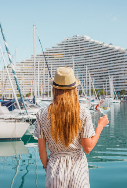金发女人在帽子站在她的背在海上，游艇，建筑物和船只的背景。在欧洲度假。不错，法国里维埃拉。旅行的照片。图片下载