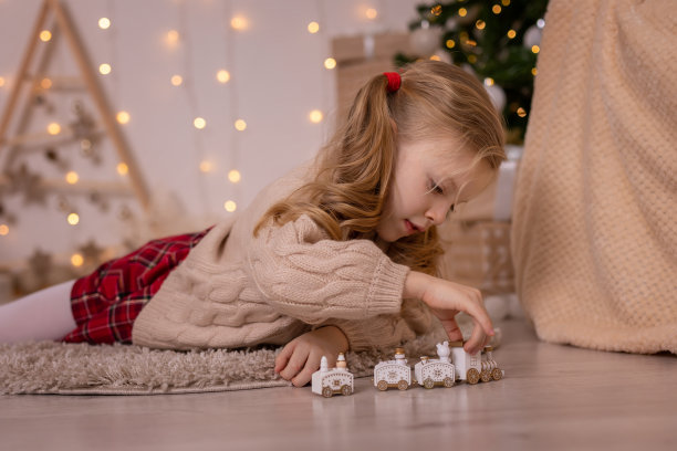 可爱的金发小女孩躺在圣诞树旁玩小火车。新年装饰。图片下载