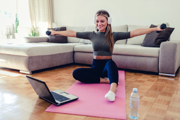 一个运动的年轻女子在家里锻炼时，用笔记本电脑和哑铃做弓步。图片下载