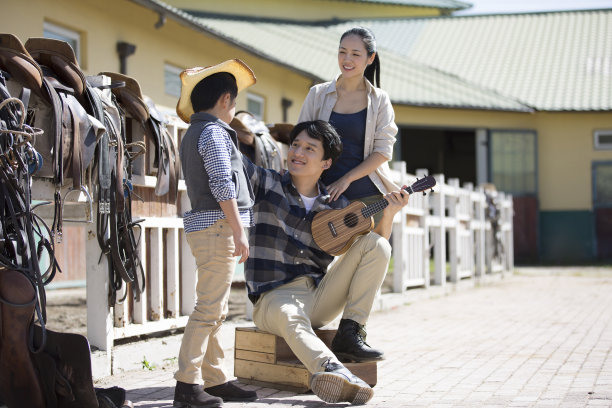 在这张太阳照片中，一家三口戴着牛仔帽在马场的护墙边弹奏尤克里里琴图片下载