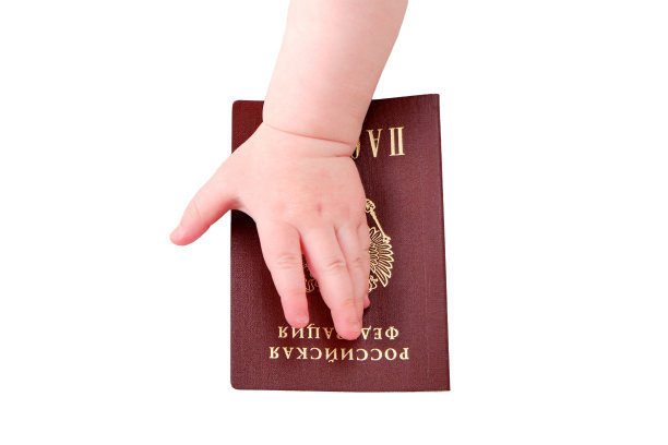 一个刚学会走路的小男孩手里拿着一本俄罗斯护照，孤零零地放在白色背景上。一个孩子拿着证明俄罗斯公民身份的文件，特写图片下载