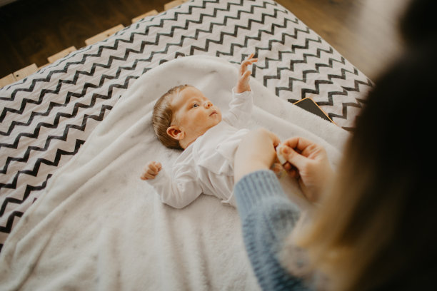 一个刚出生的男婴躺在床上，他的妈妈正在给他换尿布图片下载