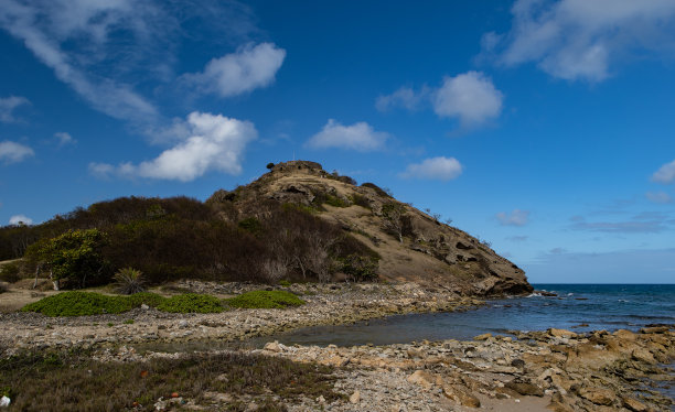 阳光明媚的日子里，海滩上的岩石和蓝天下长满绿草的小山的美丽照片图片下载