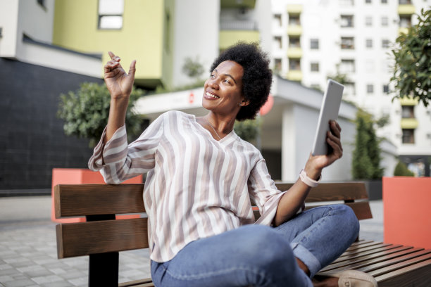 黑人妇女的肖像使用她的数字平板电脑和坐在公园的长椅上图片下载