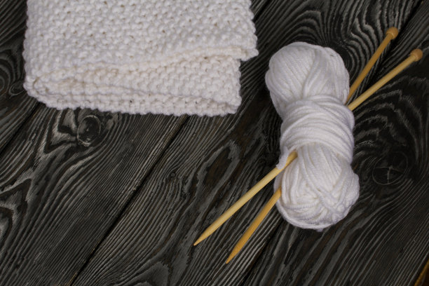 白色针织围巾。女式手工针织服装。旁边有一捆用来编织的白线和针织针。在黑板上。图片下载