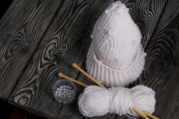 白色针织围巾。女式手工针织服装。旁边有一捆用来编织的白线和针织针。在黑板上。图片下载