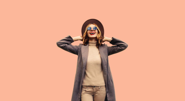 美丽的微笑的年轻女子模特穿着棕色圆帽子和米色背景外套的肖像图片下载