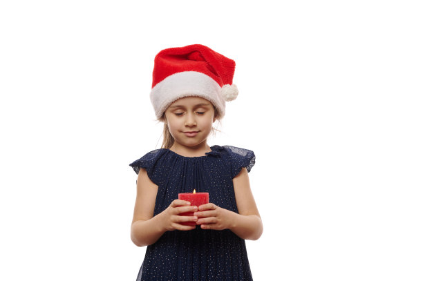 可爱的小女孩戴着圣诞帽，穿着优雅的晚礼服，在烛光下，孤独的白色背景下，许下美好的愿望图片下载