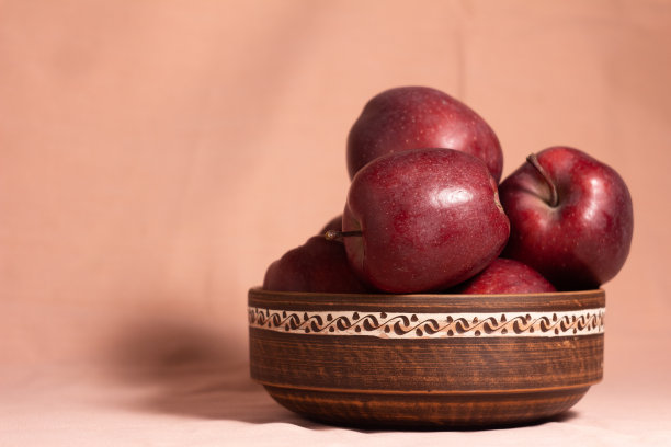 黑色的陶制碗，上面有装饰物和红苹果——红色的酋长在粉红色的背景上图片下载