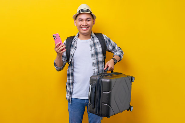 开朗的年轻旅行者旅游亚洲人，便服帽子，背包，手提箱和手机孤立在黄色背景。空中飞行旅程概念图片下载