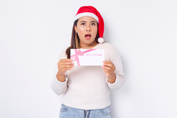 惊讶的年轻亚洲女子20岁在帽子圣诞节收到礼券券卡孤立在白色工作室背景。圣诞快乐概念图片下载