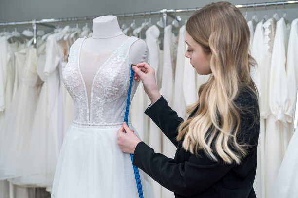 迷人的女售货员在时尚的黑色西装测量婚纱用卷尺图片下载