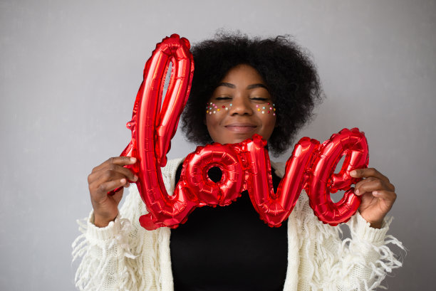 灰色背景上有一个快乐的非裔美国女孩，她拿着一个写着“爱”的气球。图片下载