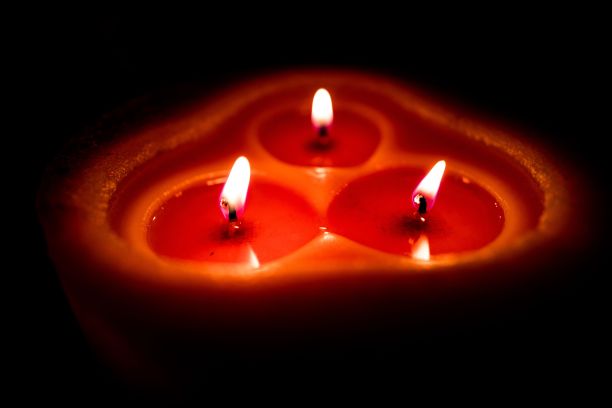 特写三闪电橙红色蜡烛与黄色火焰在黑暗的背景图片下载