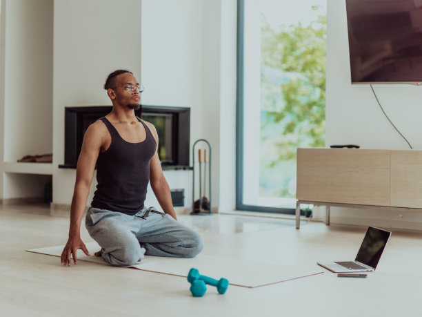 在家训练。运动男人一边训练一边在笔记本电脑上看在线教程，在客厅锻炼，自由空间图片下载