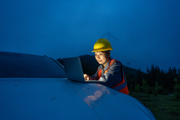 一名女工人晚上在风力发电场的汽车前使用电脑工作图片下载