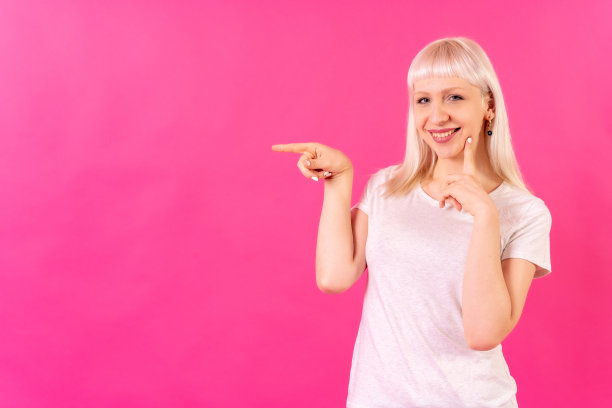 金发白人女孩工作室拍摄的粉红色背景，复制空间，微笑指向左边图片下载