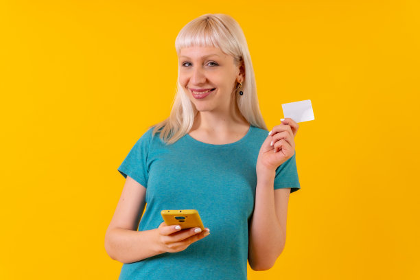网上购物用手机，金发白人女孩在工作室在黄色背景图片下载