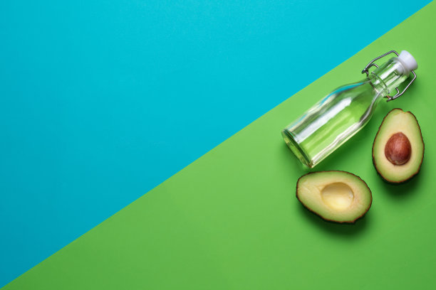 蓝色和绿色背景上的新鲜牛油果。一瓶鳄梨油。健康饮食。图片下载