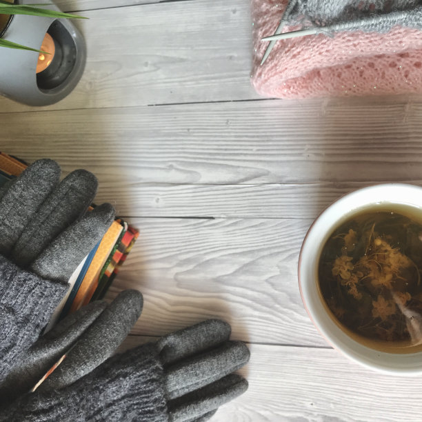 在灰色的背景上，花茶挨着针织衫，书旁边是一支香薰蜡烛，上面放着手套图片下载