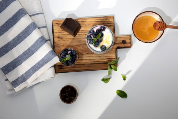 酸奶装在玻璃罐里，配上格兰诺拉麦片、巧克力、蓝莓和蜂蜜，放在木板上，白色背景上放上薄荷叶图片下载