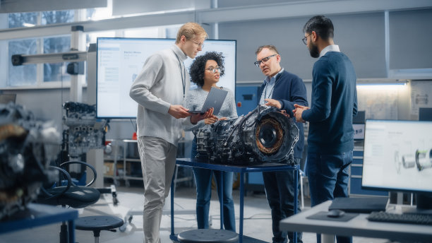 多民族青年专家与总工程师对话。专业人士使用笔记本电脑和工作在电动发动机设计。科学启动未来可持续能源解决方案。图片下载