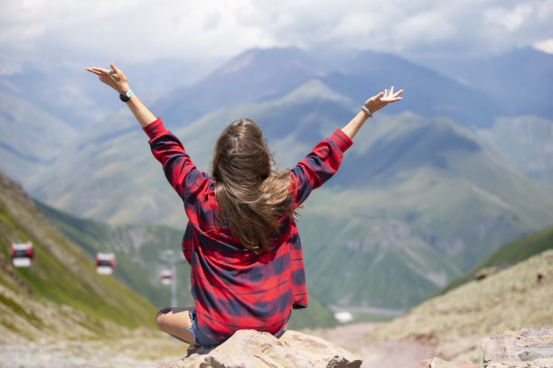 快乐的女游客在山顶上举起双手，欣赏着美丽的山景。图片下载