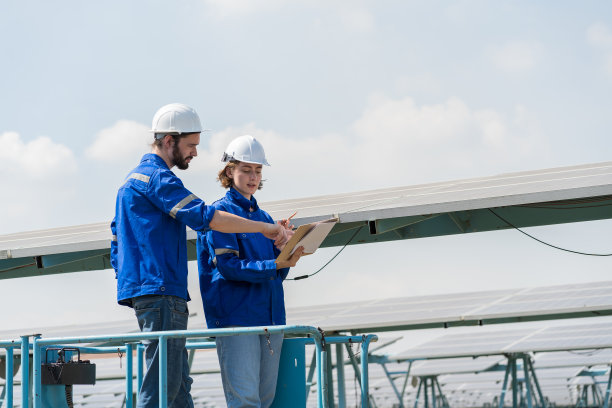 两名男性和女性电工工人在太阳能电池板发电厂的长排光伏太阳能电池电池板之间工作图片下载
